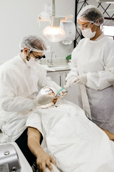 Dentist and dental hygienist wearing white scrubs cleaning a patient's teeth