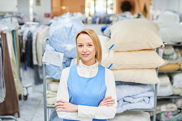 smiling woman with arms crossed standing in front of clean bed linens