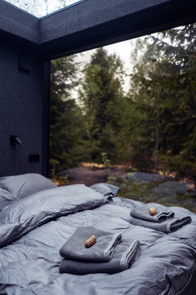 bed with grey sheets and towels overlooking forest
